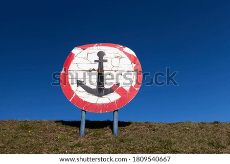 round sign with a red color and an anchor drawn inside, installed on the Bank of a river or lake in the city area, spring weather, river transport handling traffic order signs, old sign