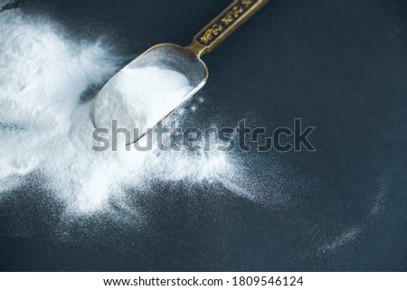 Glass bowl of baking soda. Spoonful of bicarbonate. Top view, flat lay. Close up on a black background. copy space for text.