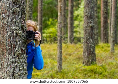 Young woman trekking among trees and taking pictures with camera. middle age woman photographer taking picture in autumn forest. Nature photography.