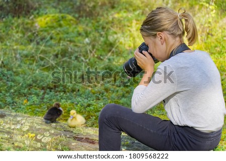 Young girl takes pictures of cute ducklings in the forest. Learning in photographing children, trainee in nature. young girl learning to photograph