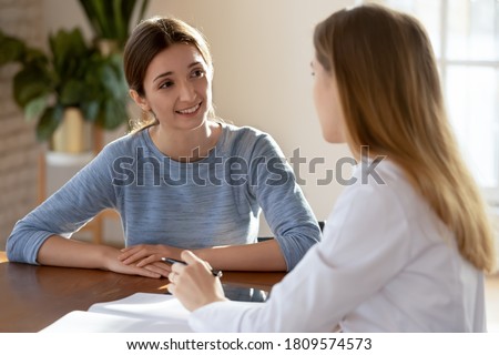 Smiling young woman listening to doctor therapist at meeting, sitting at work table in hospital, physician consulting patient about checkup results, giving recommendations at medical appointment Royalty-Free Stock Photo #1809574573