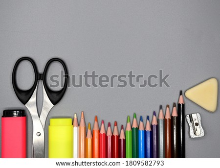 School supplies, colored pencils, pencil sharpener, eraser, markers and scissors at the bottom, gray background.