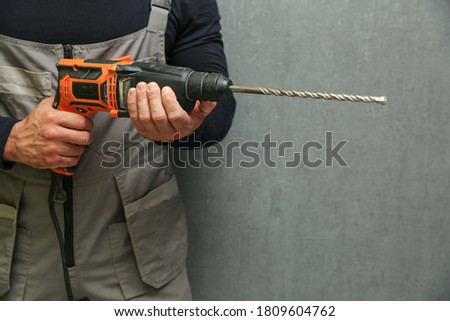 man's hand holds hammer drill on the background of gray wall with copy space