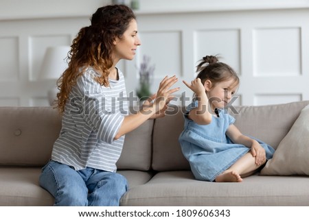 Single mother and little kid sit on couch at home, parent scolds preschool daughter teaches naughty mischievous child. Concept of punishment, bad behaviour misbehave of infant, upbringing difficulties Royalty-Free Stock Photo #1809606343