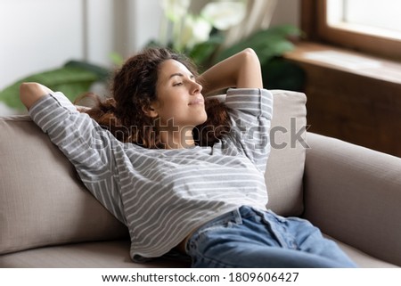 Peaceful young woman relaxing alone in cozy living room leaned on sofa cushion breath fresh air looks into distance, day dreaming, admires city view through window spend lazy free weekend time at home Royalty-Free Stock Photo #1809606427