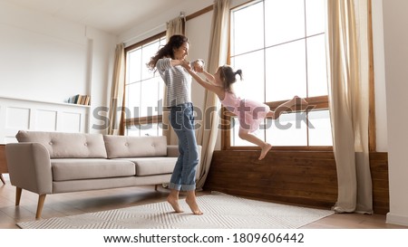 Full length happy mother holds hands spinning carefree adorable little daughter listen music moving in modern interior light cozy living room. Active funny games, lively play have fun together at home Royalty-Free Stock Photo #1809606442