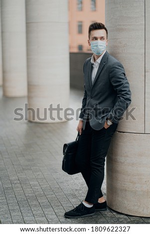 young man Manager, wearing a face mask blue color protective against virus, germs, covid19. He is dressed in a classic grey suit, a fashionable hair salon.