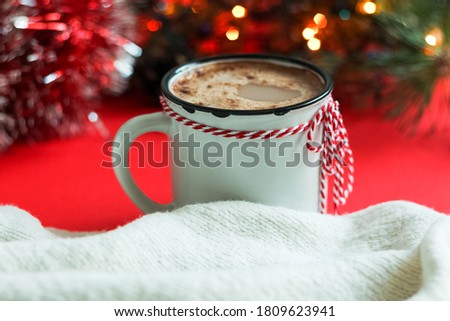 White mug with cappuccino, knitted scarf and garland on red background.