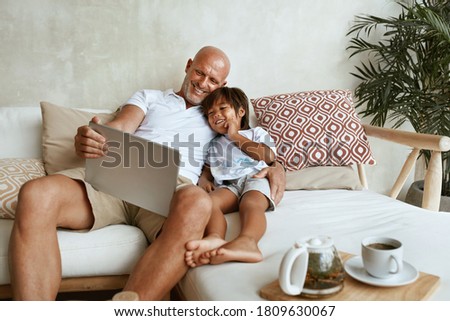 Father And Son With Tablet Portrait. Mixed Race Family Of Dad And Little Boy Using Portable Digital Device Sitting On Sofa Together. Technology For Education And Fun At Tropical Resort.