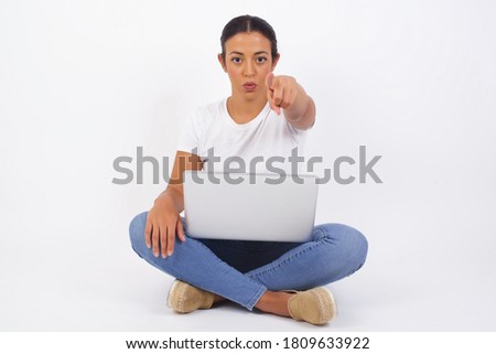 Indoor shot of cheerful young woman using computer in casual clothes indicates happily at you, chooses to compete, has positive expression. beautiful clever student makes choice, isolated on gray Wall