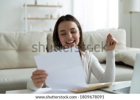 Overjoyed young woman reading paper letter with good news, celebrating last mortgage payment. Happy emotional millennial lady making yes gesture, feeling excited by loan approval in post mail.