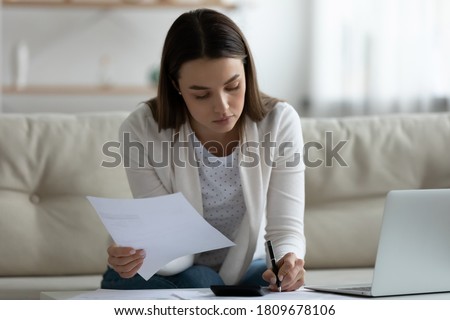 Focused young woman holding paper banking notification, planning mortgage payments alone at home. Serious concentrated millennial girl managing financial expenditures on medical services or study. Royalty-Free Stock Photo #1809678106