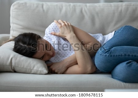 Stressed young woman lying on sofa, embracing shoulders with arms, suffering from depression alone at home or caught cold and shivering. Unhappy girl feeling unwell, mourning yearning indoors. Royalty-Free Stock Photo #1809678115