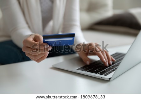 Close up young woman holding plastic banking credit debit card, involved in online shopping on computer at home. Female client entering payment information cvv code confirming purchase indoors. Royalty-Free Stock Photo #1809678133