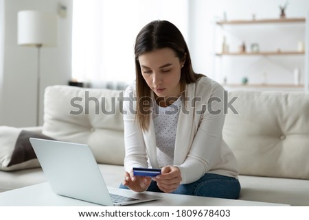 Focused young woman entering banking credit card information in computer application, making household payments online, booking flight tickets or hotel, purchasing goods or confirming transaction. Royalty-Free Stock Photo #1809678403