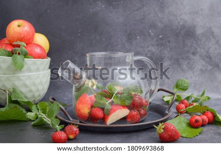 Glass teapot with fruits, berries and herbs on the tray. Horizontal frame. Grey background.