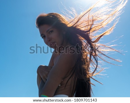 dark-skinned woman in white shorts with long hair poses for photographer on river bank against background of waves