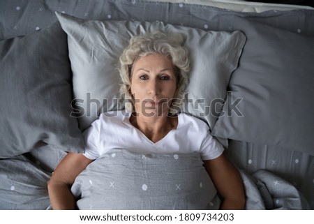Top view close up sleepless upset senior mature woman with open eyes lying in bed under blanket, trying to sleep, depressed frustrated middle aged female suffering from insomnia, health problem Royalty-Free Stock Photo #1809734203