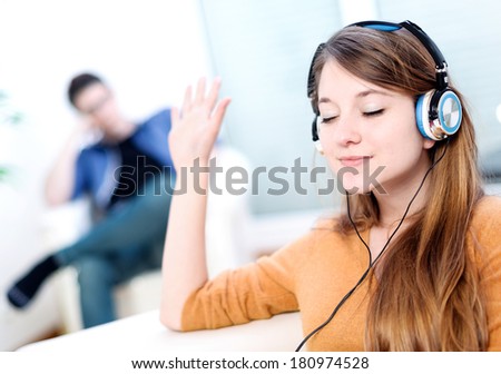 Beautiful blond listening to some music while her boyfriend is bored