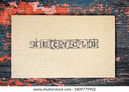 Cardboard with word Recycle made by black alphabet stamps on old wooden background.