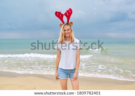 Beautiful smiling happy young woman, teenage girl walking on the beach in Christmas deer ears. New Year holidays, vacations, travel, tourism concept