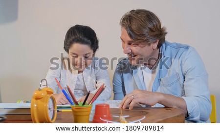 Father and daughter spend quality time together painting, painting. The little girl is painting the picture in the coloring book with her father. Concept of family time together on Father's Day.
