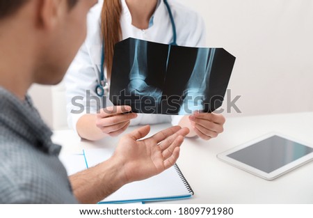 Orthopedist showing X-ray picture to patient at table in clinic, closeup