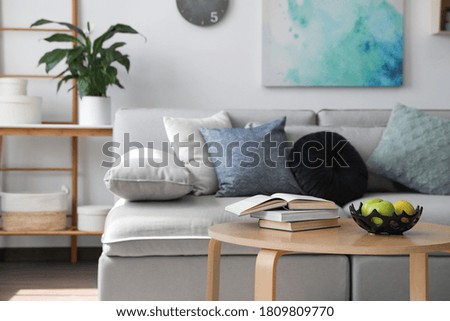 Table with books and apples near sofa in living room. Interior design