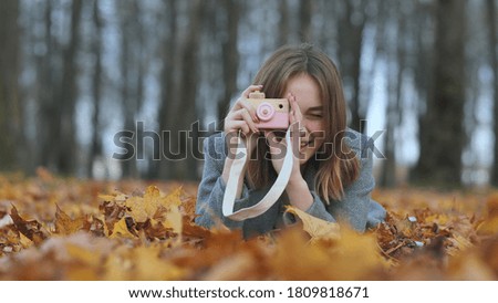 A young beautiful girl takes pictures in an autumn park using a toy camera.