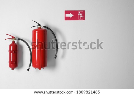 Different fire extinguishers and emergency exit sign on white wall. Space for text