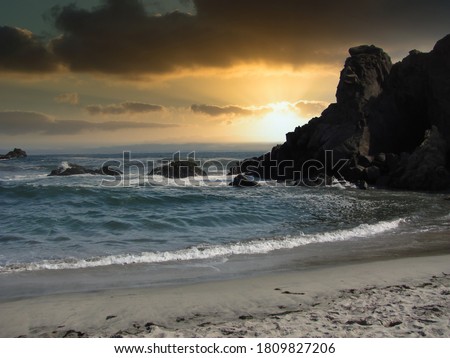 Dramatic beach sunset with rocks jutting out of the surf.                               