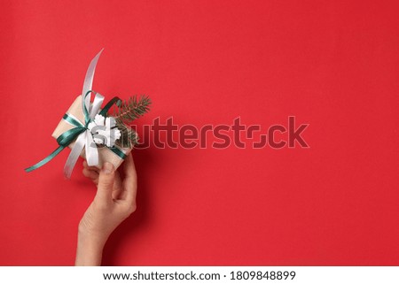 Woman holding giftbox of kraft paper with ribbons on red background. Greeting Xmas card. Boxing day. View from above
