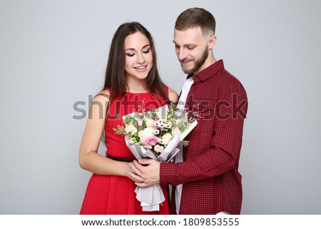 Happy young couple with bouquet of flowers on grey background
