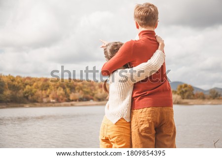 back view of preteen kids, boy and girl hugging in fall park with lake.  Friends wearing warm knit sweaters