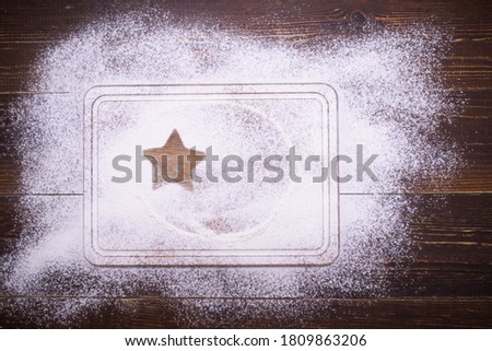The outline of a star on a surface covered with white powder. Flour is scattered on a wooden table and a cutting board.  