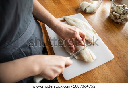 Woman cutting fresh fish fillet in domestic kitchen