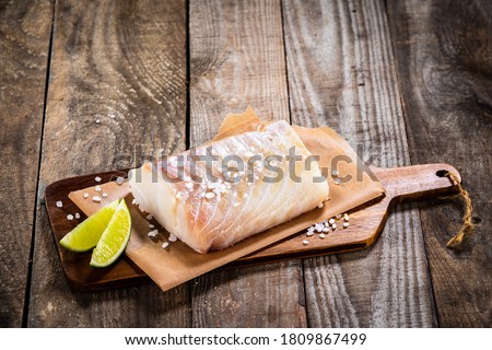 Fresh raw cod with lemon on cutting board on wooden table