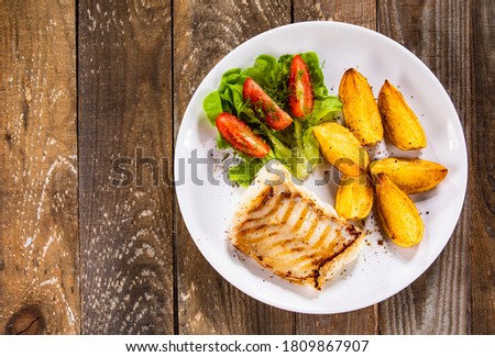 Fish dish - fried cod fillet with potatoes and vegetable salad on wooden table