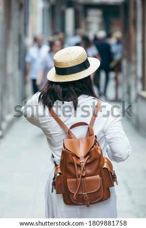 woman in white clothes in straw hat and brown leather backpack walking by city street