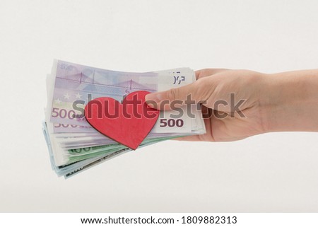 in his hand are Euro notes and a red heart. hand gives money to donate to heart donors CSR concept, health care, organ donation, family insurance world heart day, world health Day Royalty-Free Stock Photo #1809882313