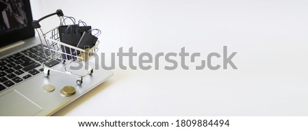 Shopping cart with bags stand on laptop. Ordering  in the internet store. White background. Black friday banner. Sale announcement. E-commerce business. Copy space 
