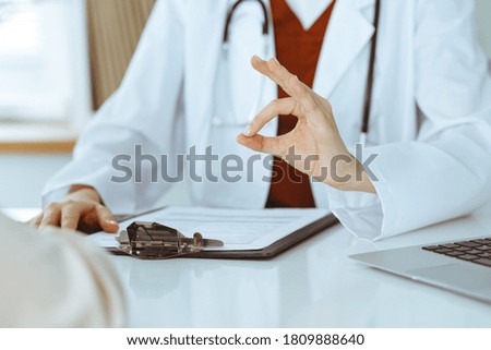 Unknown woman-doctor and patient discussing something while sitting at the table in clinic, close-up. Medicine concept