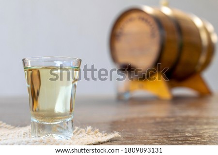 glass of high quality distilled alcohol and defocused old oak barrel in the background. Cachaça is a typical drink from Brazil, also known as aguardente. September 13 is the national day of cachaça. Royalty-Free Stock Photo #1809893131