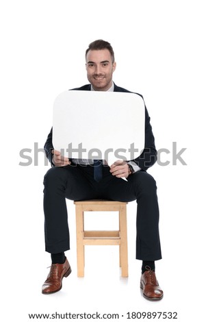 Happy businessman smiling and holding speech bubble while sitting on a chair on white studio background