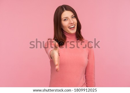 Nice to meet you. Friendly smiling woman in pink sweater stretching her hand welcoming guests, hospitality. Indoor studio shot isolated on pink background