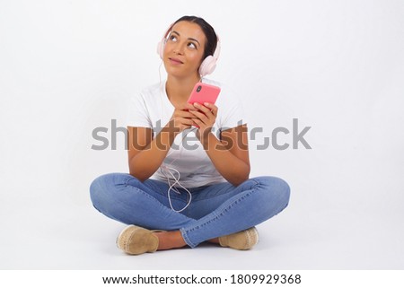 Image of a happy young beautiful woman posing isolated over bright background listening to music with earphones using mobile phone.