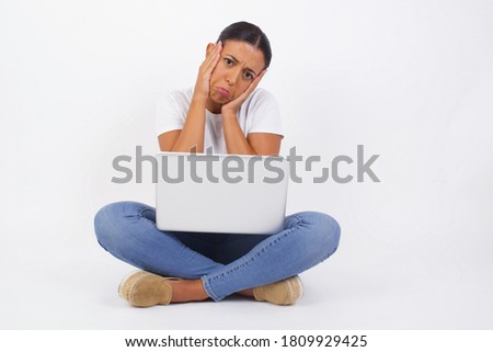 Portrait of beautiful young woman using laptop holding head in hands with unhappy expression watching sad movie about animals and trying not to cry.