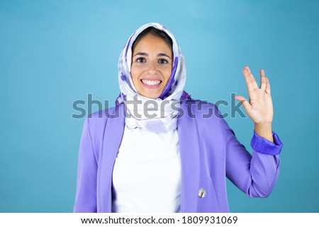 Young beautiful arab woman wearing islamic hijab over isolated blue background doing hand symbol