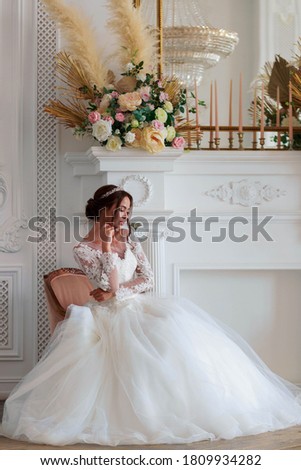 The bride in a white wedding dress sits thoughtfully in a chair waiting for the groom.
