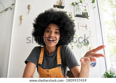 Young African American hipster woman with Afro hair looking at webcam talking to camera with friend online sitting at cafe table making video call, virtual chat, recording blog, headshot portrait.
